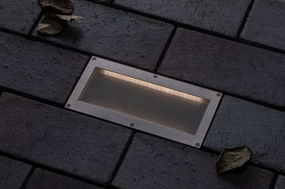 Recessed LED floor light in brushed stainless steel with warm white light on dark paving stones.