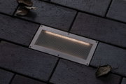 Recessed stainless steel LED floor light with warm white glow on dark paving stones