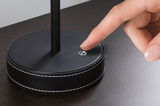 Base ronde noire de lampe en cuir avec couture blanche, doigt touchant un petit interrupteur.