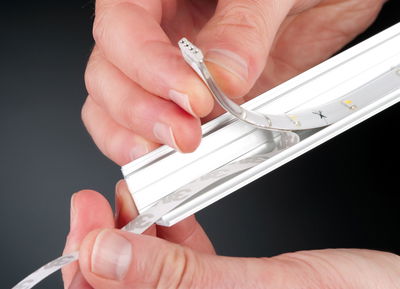 Hand legt flexible weiße LED-Lichtleiste mit Aluminiumprofil und 3M-Klebeband an für Beleuchtung