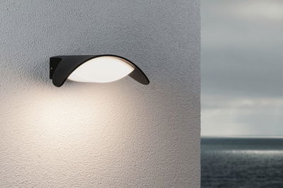 Modern black outdoor wall light with white diffuser on grey wall, ideal for garden lighting solutions.