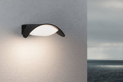 Moderne schwarze Außenwandleuchte mit weißem Diffusor an grauer Wand, geeignet für Gartenbeleuchtung.