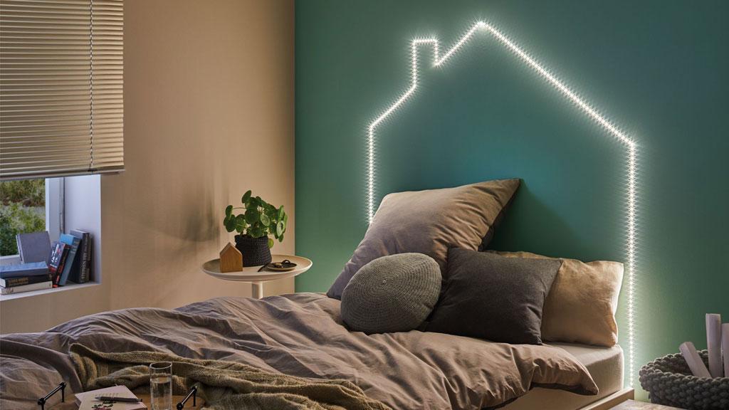 Gemütliches Schlafzimmer mit LED-Lichtband in Hausform an grüner Wand für moderne Wohnraumbeleuchtung.