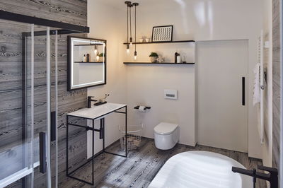 Modern bathroom with wood-look walls, white sink on black metal frame, LED mirror and hanging pendant lights