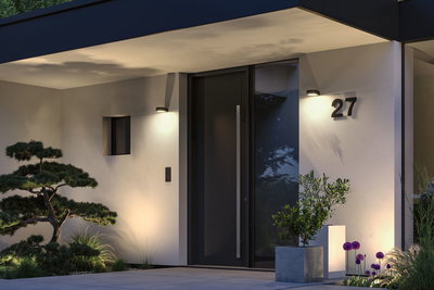 Moderner Hauseingang mit schwarzer Tür, weißer Fassade und warmweißen Außenwandleuchten für stimmungsvolle Beleuchtung.
