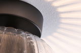 Ceiling light with black metal base and ribbed clear glass, decorative light patterns on wall