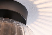 Deckenleuchte mit schwarzem Metallfuß und geriffeltem transparentem Glas, dekorative Lichtmuster an Wand