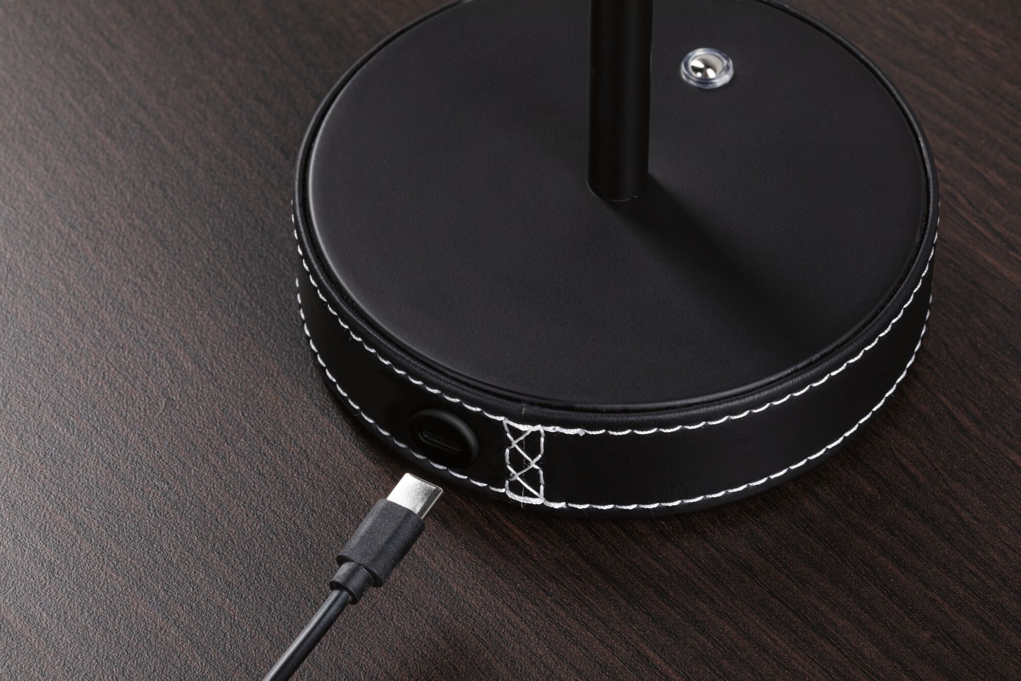 Base de lampe ronde en cuir noir avec couture blanche et port USB-C sur surface en bois foncé