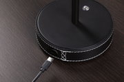 Schwarze runde Lampenbasis aus Leder mit weißer Naht und USB-C Anschluss auf dunklem Holztisch