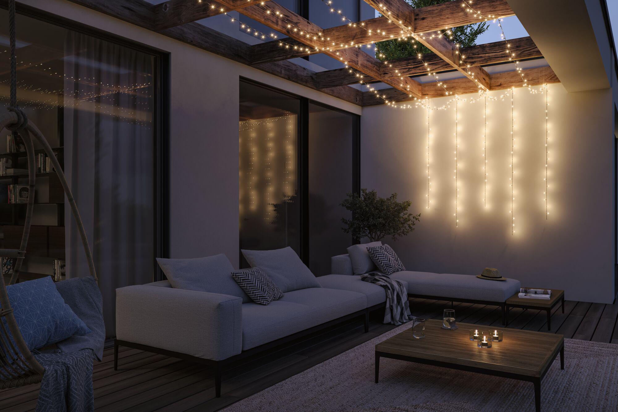 Gemütliche Terrasse mit grauem Polstersofa und warmweißen LED-Lichterketten an Holzbalken