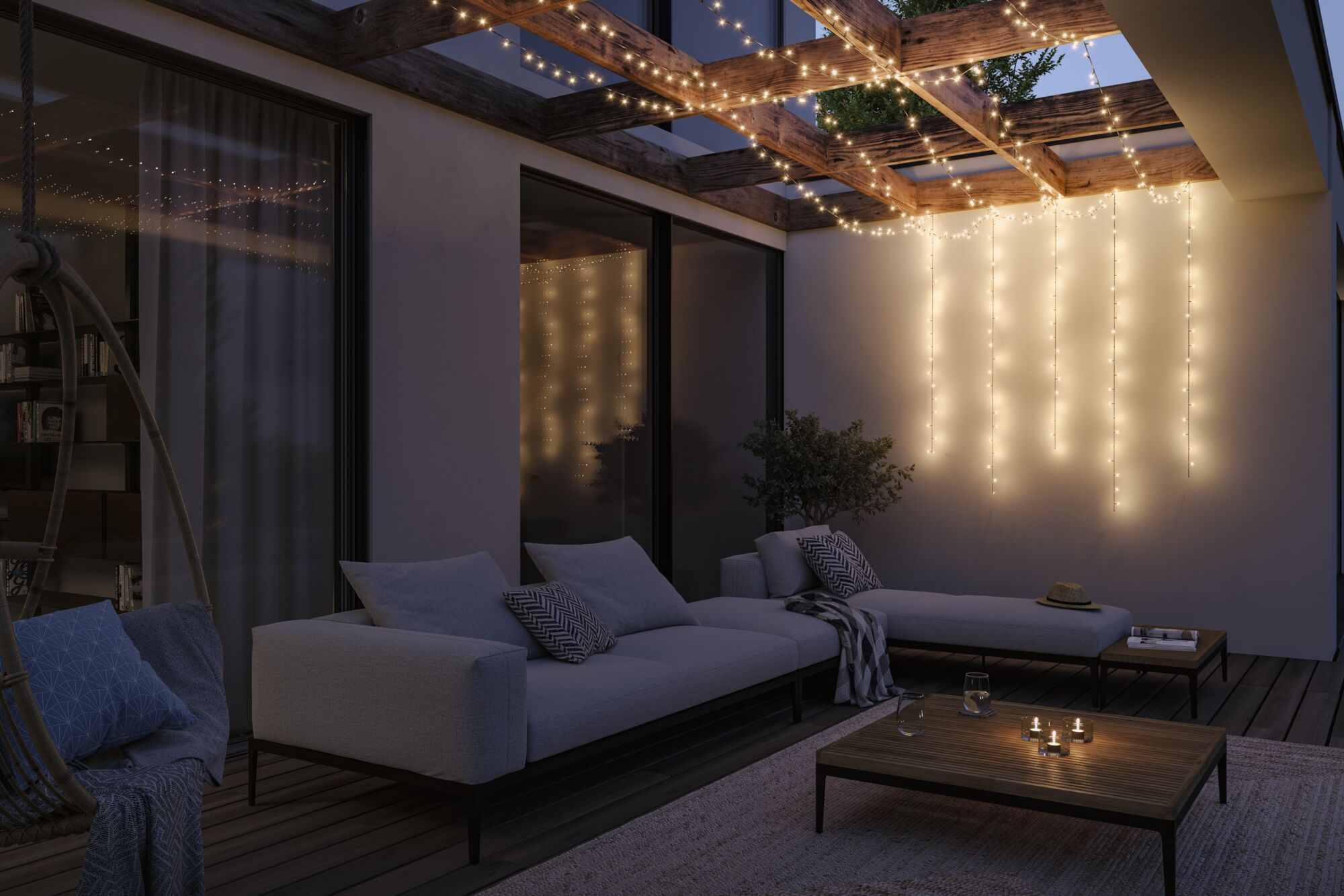 Gemütliche Terrasse mit grauem Polstersofa und warmweißen LED-Lichterketten an Holzbalken