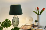 Table lamp with green velvet shade and faceted glass base beside white vase with tulips and clock