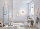 Modern living room with white plastic chair, round LED wall lights, and light wooden floor.
