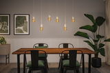Moderner Essbereich mit Holz-Tisch, schwarzen Metallstühlen und warmen LED-Glühbirnen als Pendelleuchten