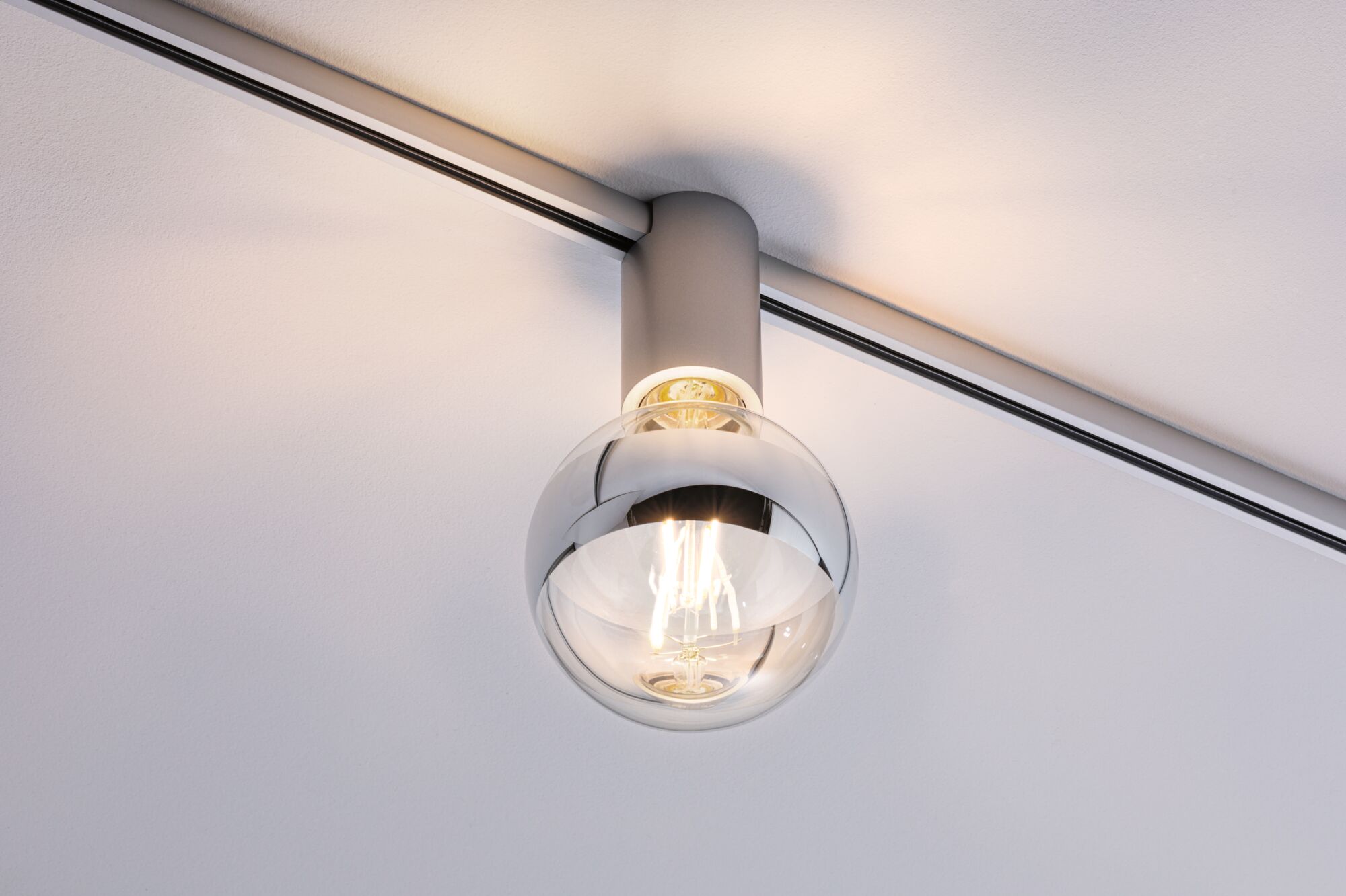 Moderner Deckenstrahler mit klarem Glaskugel-Schirm und silbernem Metallgehäuse für Schienensystem.