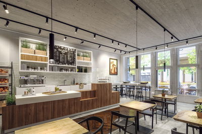 Modernes Café mit Holztheke, weißen Fliesen und schwarzen Pendelleuchten für gemütliche Atmosphäre.