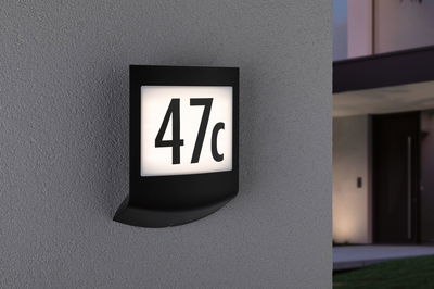 Black LED house number light with white illuminated panel showing number 47c on grey wall