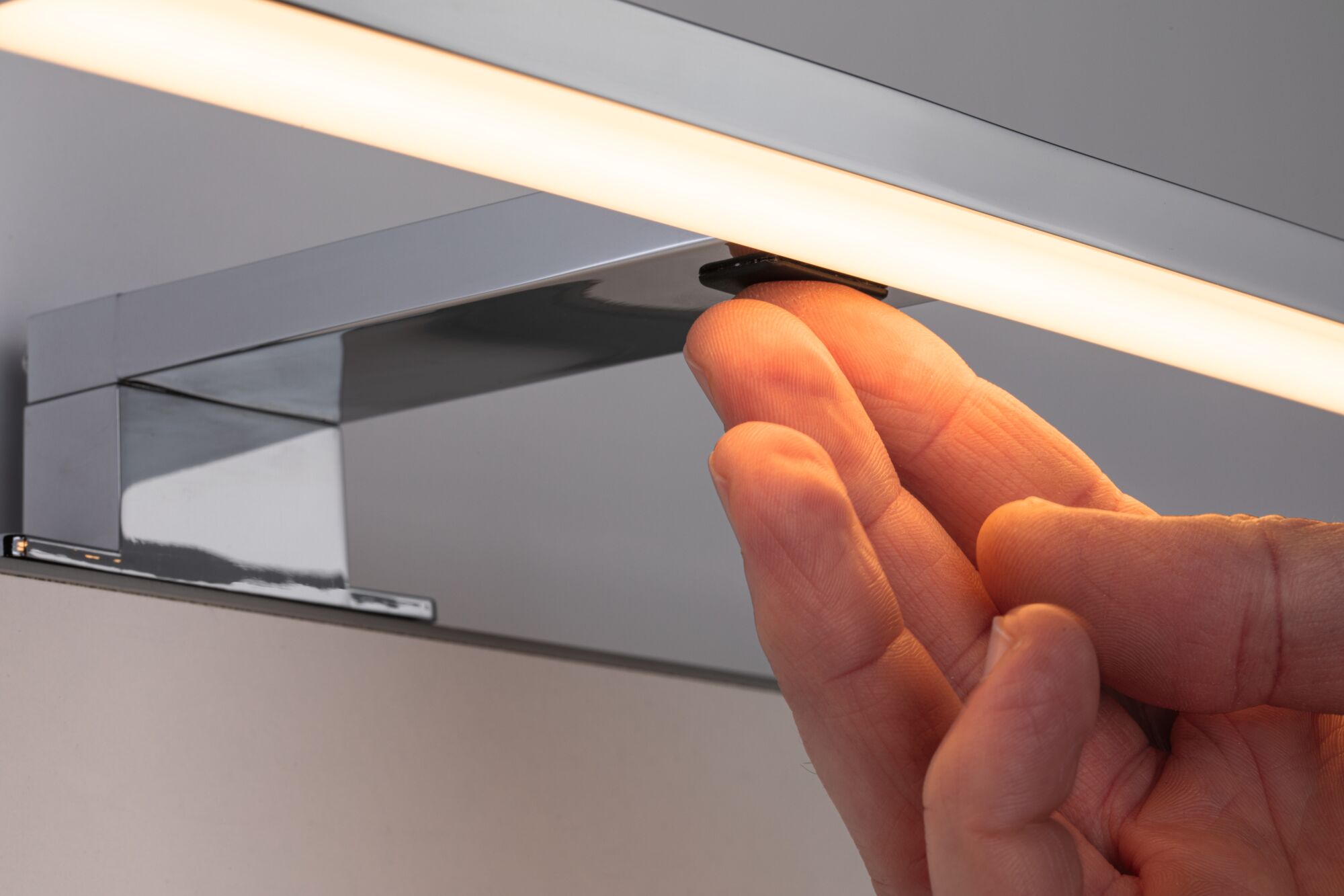 Main réglant une lampe miroir LED chromée avec lumière blanche chaude pour salle de bain