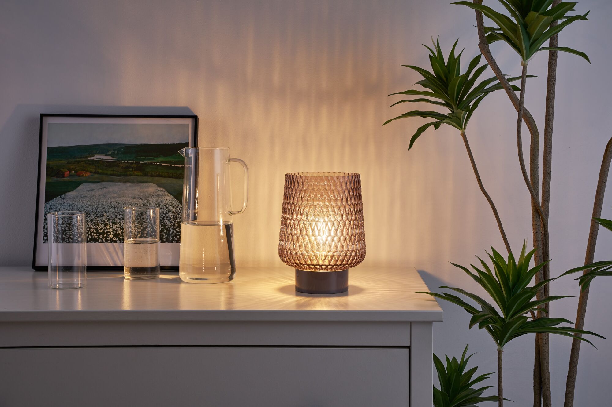 Lampe de table en verre brun à motif sur buffet blanc avec pichet d'eau et plante verte d'intérieur