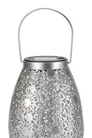 Silver metal lantern with intricate pattern and solar panel on top for outdoor lighting decoration