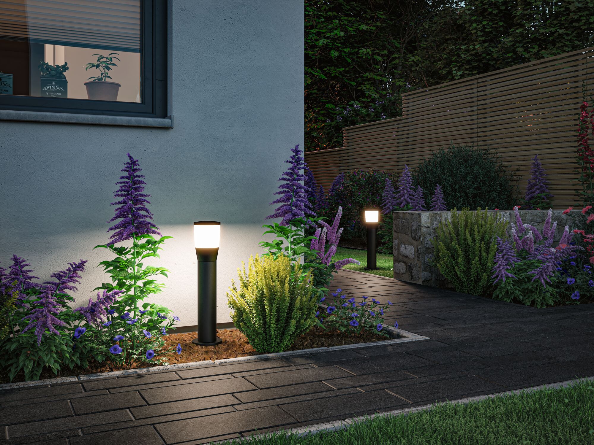 Moderne zwarte buitenlampen met warm wit licht verlichten tuinpad met paarse bloemen en stenen muur.