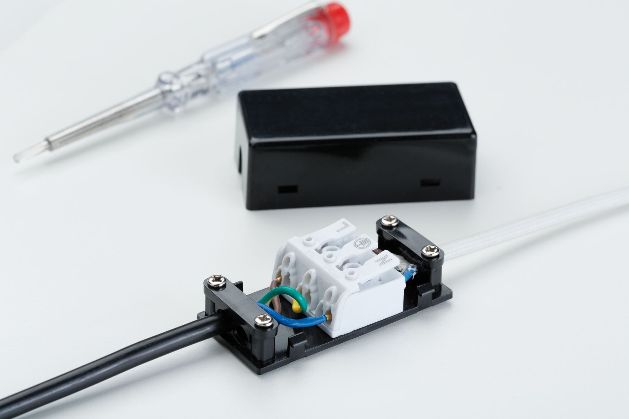 Elektrische aansluitdoos met zwarte en witte kabels, schroevendraaier op de achtergrond voor lichtinstallatie