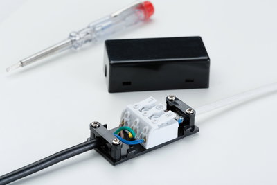 Electrical connection box with black and white cables, screwdriver in background for lighting installation