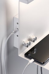 White wall shelf with two silver knobs and smartphone charging via USB cable
