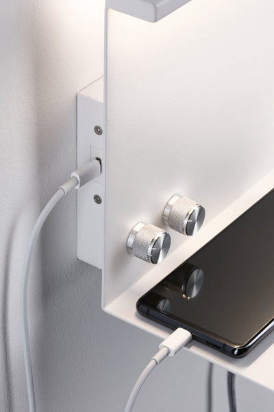 White wall shelf with two silver knobs and smartphone charging via USB cable