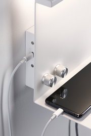 Weißes Wandregal mit zwei silbernen Drehknöpfen und Smartphone, das per USB-Kabel geladen wird