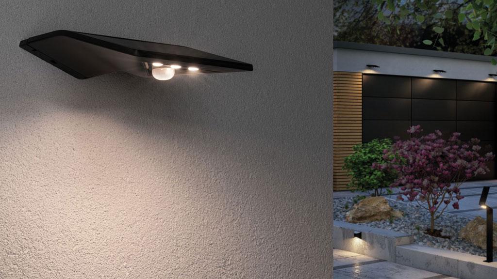 Sort LED-væglampe med bevægelsessensor oplyser havegang og indkørsel udendørs om natten.