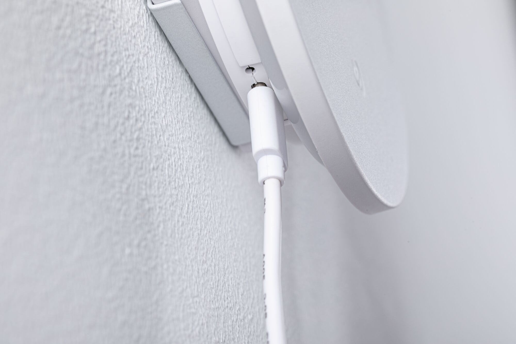Close-up of white cable connection on white wall mount for electronic device installation