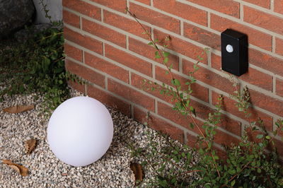 White plastic globe light on gravel by red brick wall with black motion sensor for outdoor lighting.