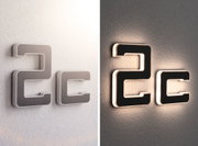 Moderne LED-Wandbuchstaben in Schwarz mit weißem Rahmen, beleuchtet und unbeleuchtet an grauer Wand.