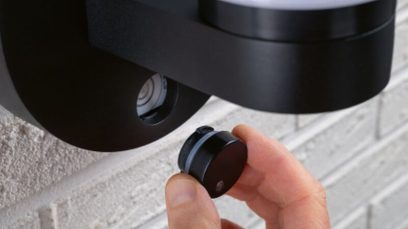Hand holding black round ModuShine metal accessory part near grey wall with lighting