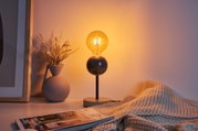 Modern table lamp with wooden base and black rod, warm light beside grey vase and blanket