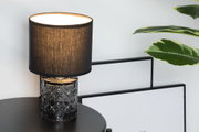 Table lamp with black fabric shade and patterned glass base on black table in modern interior