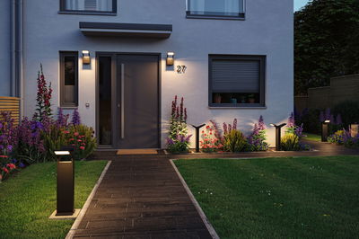 Moderner Außenbereich mit schwarzer LED-Wegeleuchte und Hauswandbeleuchtung an grauer Fassade.