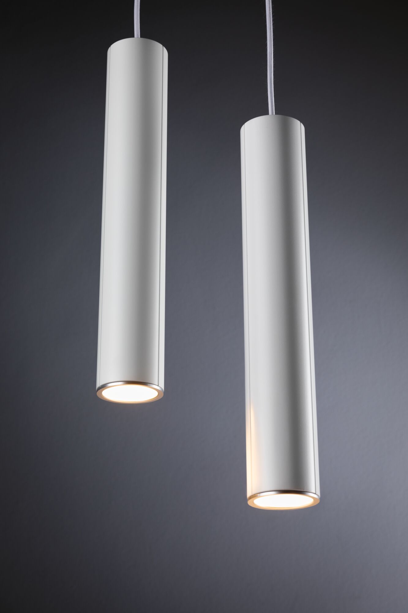 Two white cylindrical metal LED pendant lights with warm light for modern interior lighting