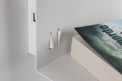 White metal shelf with two white plastic hooks and a book with dark cover on it.