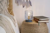 Patterned glass table lamp with warm light on woven side table next to books and cozy bedding