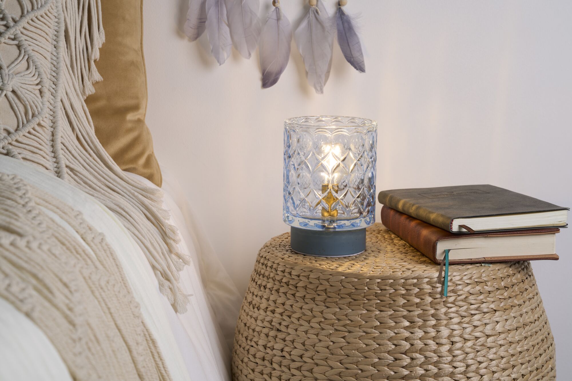 Patterned glass table lamp with warm light on woven side table beside books and cushions