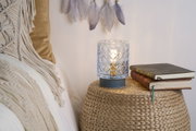 Patterned glass table lamp with warm light on woven side table beside books and cushions