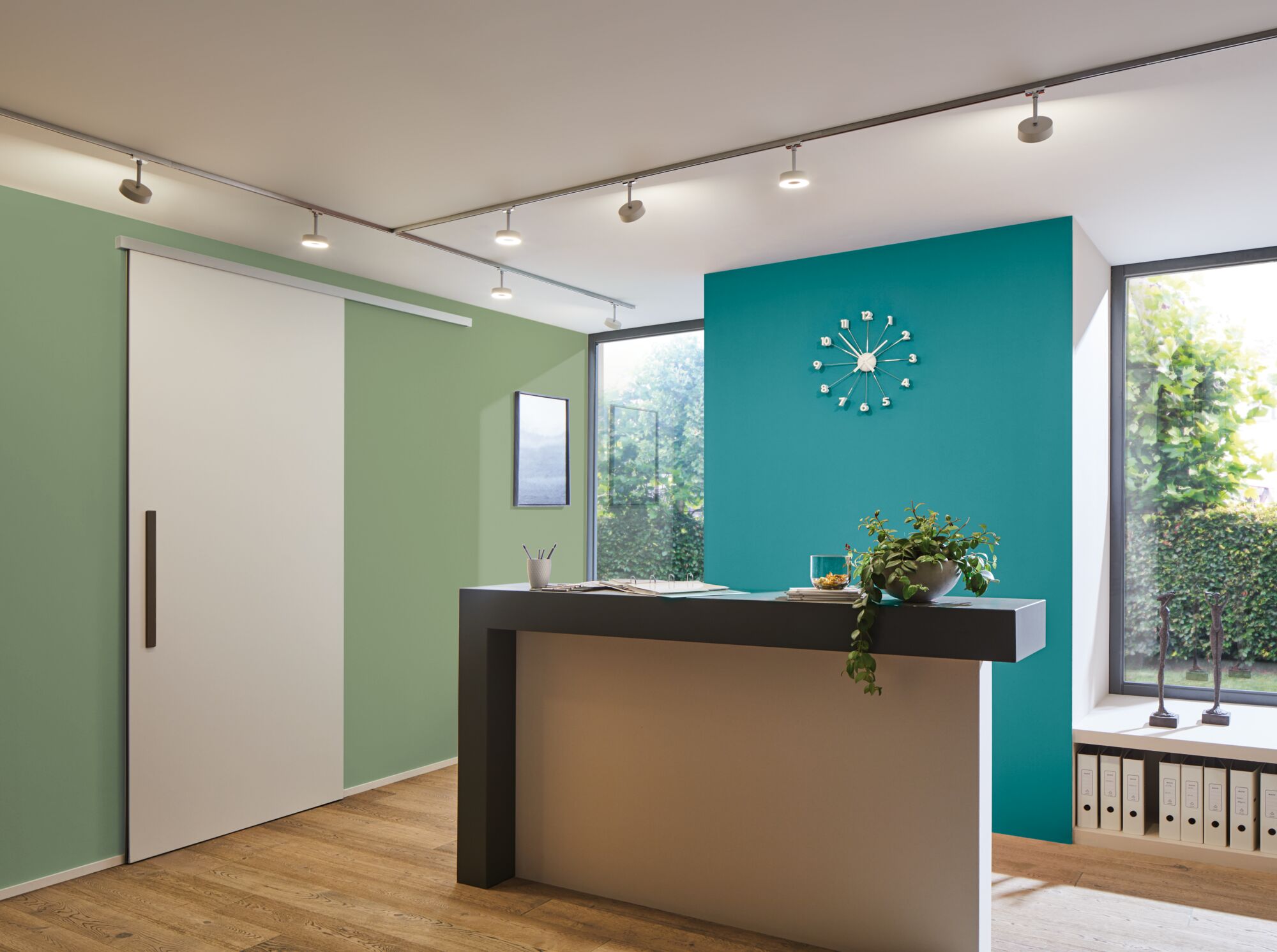 Moderner Empfangstresen in Grau vor türkisfarbener Wand mit minimalistischer Uhr und Holzfußboden