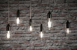 Six clear filament LED bulbs in various shapes hanging against grey brick wall for decorative lighting