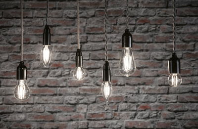Six clear filament LED bulbs in various shapes hanging against grey brick wall for decorative lighting