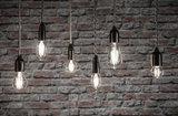 Sechs klare Filament-LED-Leuchtmittel in verschiedenen Formen vor grauer Backsteinwand für dekorative Beleuchtung