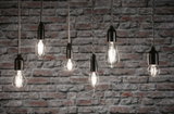 Sechs klare Filament-LED-Leuchtmittel in verschiedenen Formen vor grauer Backsteinwand für dekorative Beleuchtung
