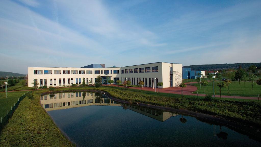 Modern kantoorgebouw met witte gevel en vijver op de voorgrond, Paulmann locatie.