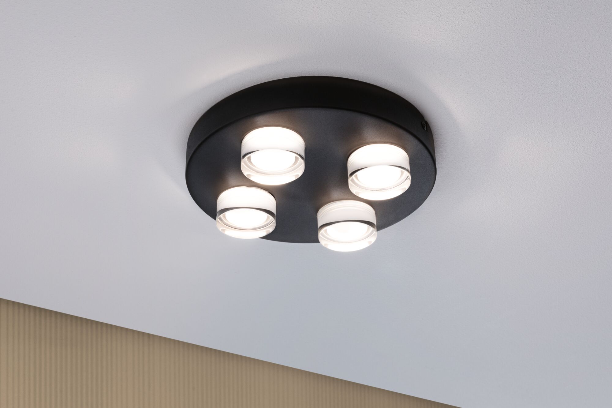 Plafonnier rond en métal noir avec quatre lentilles LED blanches pour un éclairage moderne.